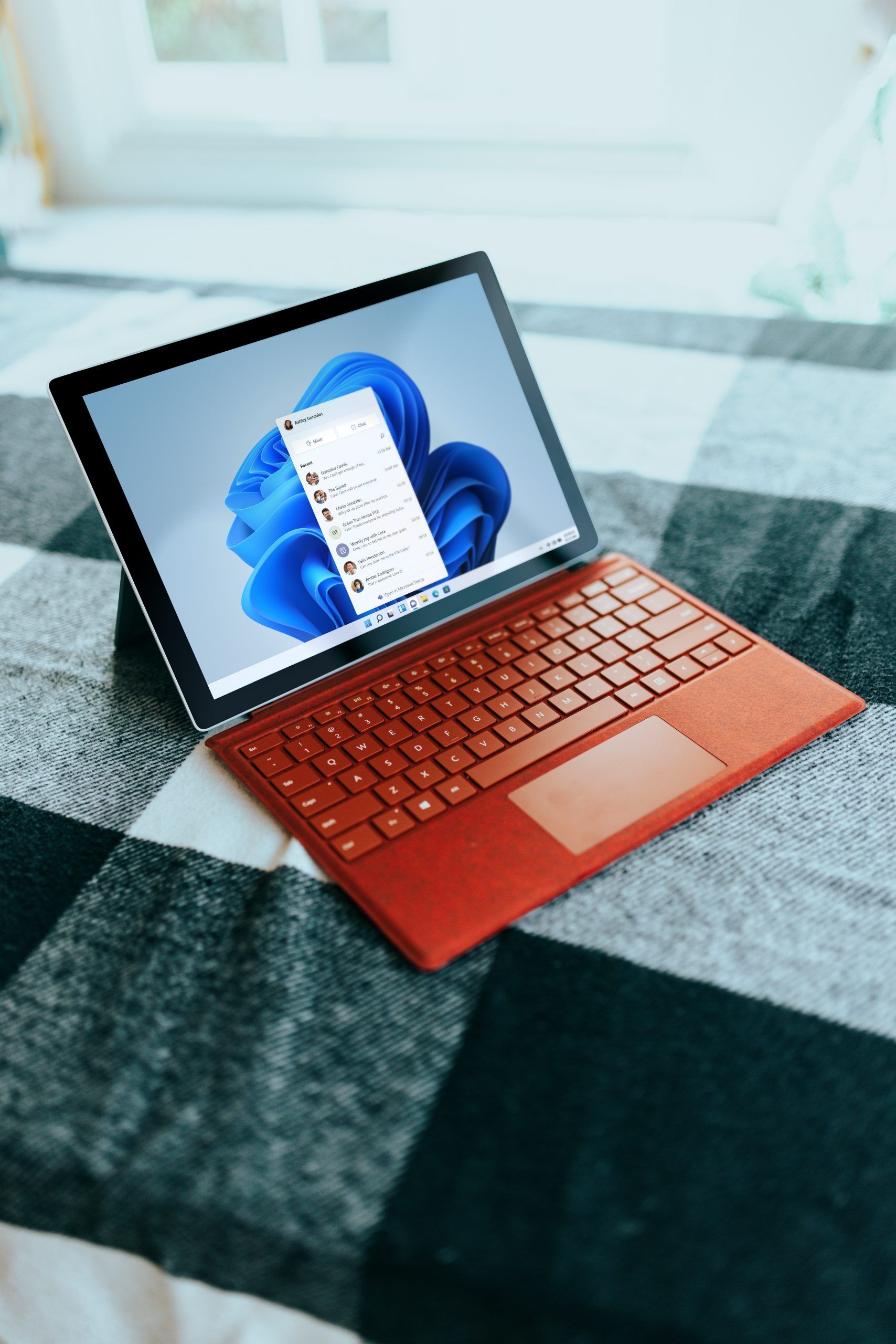 Red Surface laptop on a checkered bed by a window Red Surface laptop on a checkered bed by a window